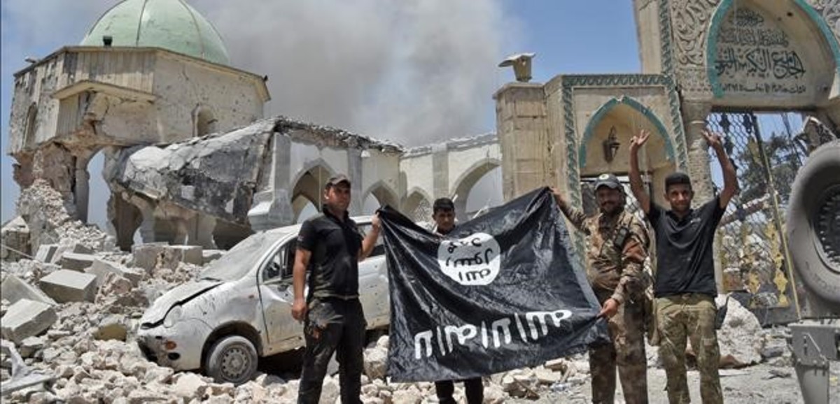 TOPSHOT - A member of the Iraqi Counter-Terrorism Service  CTS  raises the victory gesture as others hold upside-down the black flag of the Islamic State  IS  group  outside the destroyed Al-Nuri Mosque in the Old City of Mosul  after the area was retaken from IS  on June 30  2017  Explosions on June 21 evening levelled the mosque  where Abu Bakr al-Baghdadi gave his first sermon as leader of the Islamic State group and its ancient minaret  Iraq will declare victory in the eight-month battle to retake second city Mosul from jihadists in the  next few days   a senior commander said on June 30  2017  Iraqi forces launched the gruelling battle for Mosul on October 17  2016  advancing to the city and retaking its eastern side before setting their sights on the smaller but more densely populated west    AFP PHOTO   FADEL SENNA