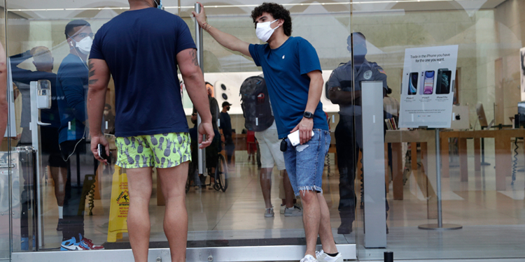 An employee wearing a protective face covering, right, monitors the flow of customers at an Apple retail store along Lincoln Road Mall during the new coronavirus pandemic, Wednesday, June 17, 2020, in Miami Beach, Fla. (AP Photo/Lynne Sladky)
