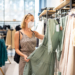 Fashionable woman wearing protective face mask shopping clothes in reopen retail shopping store. New normal lifestyle during corona virus pandemic.